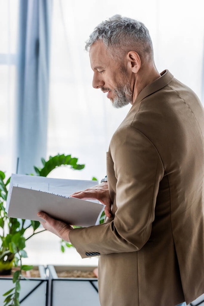 side view of bearded businessman looking at documents in folder - Photo, Image