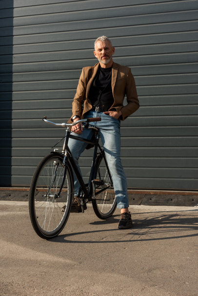 zonlicht op knappe zakenman met hand in hand bij fiets buiten  - Foto, afbeelding