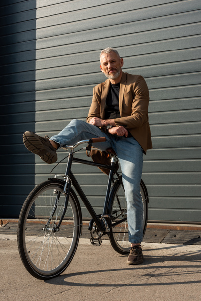 sunlight on handsome businessman posing near bicycle outside  - 写真・画像