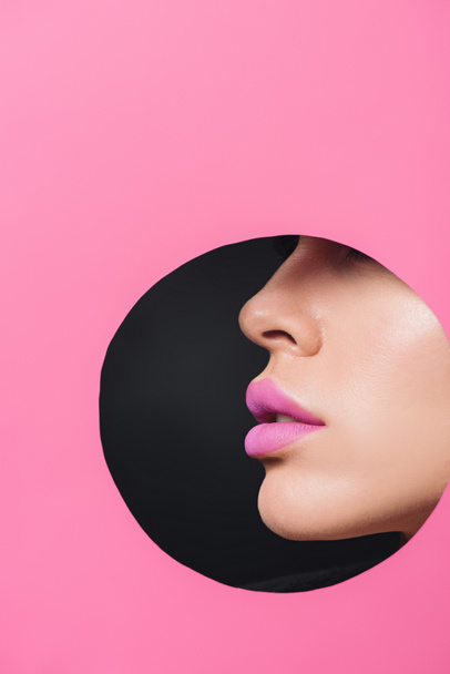 Partial view of female face with pink lips in round hole in paper on black  - Foto, Imagem