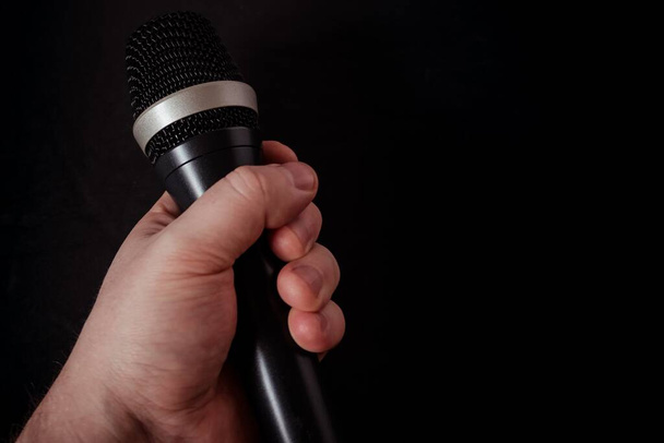 A closeup shot of a microphone in the hand of a person on a black background - Foto, imagen