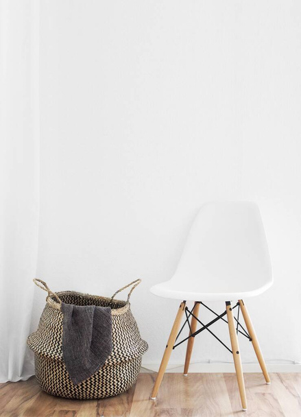 A vertical shot of a white chair and a basket for clothes in front of a white wall - Fotó, kép