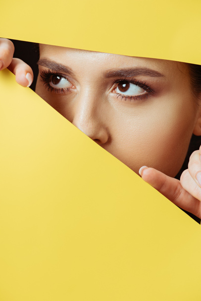 Woman looking away across hole and touching yellow paper with fingers - Fotó, kép