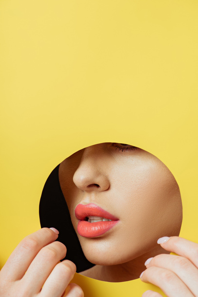 Cropped view of woman with coral lips touching yellow paper with hands on black - Фото, зображення