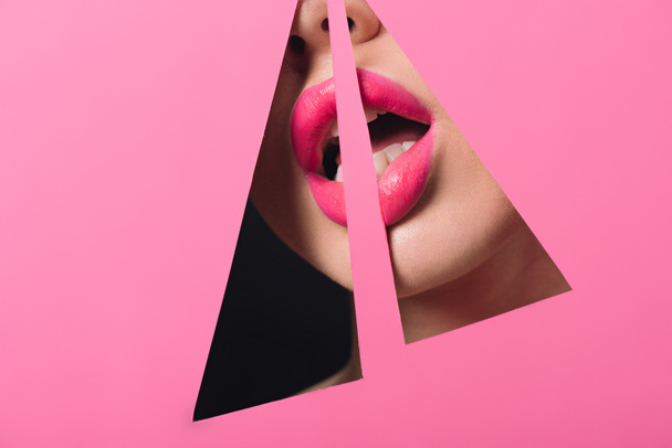 Cropped view of woman with pink lips and open mouth across triangular holes in paper on black - Foto, Bild