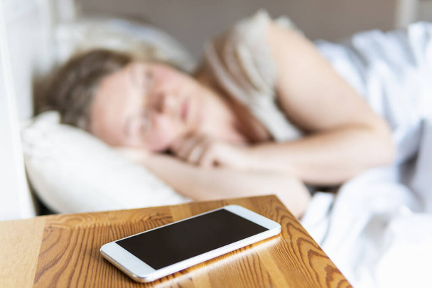 Mladá východoevropská žena spící v posteli s mobilním telefonem v popředí. - Fotografie, Obrázek