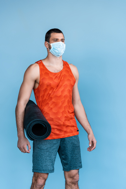 sportos férfi orvosi maszk áll fitness mat elszigetelt kék  - Fotó, kép