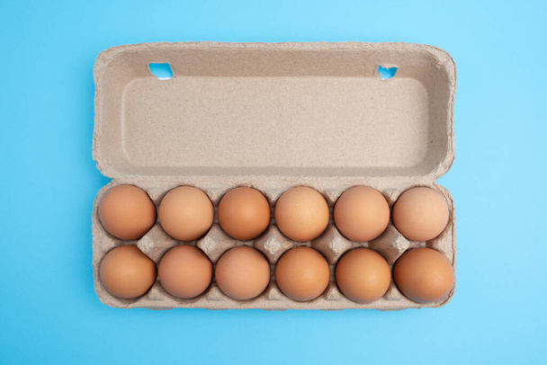 Dozen eggs in open carton on blue background. Top view with copy space - Foto, Imagen