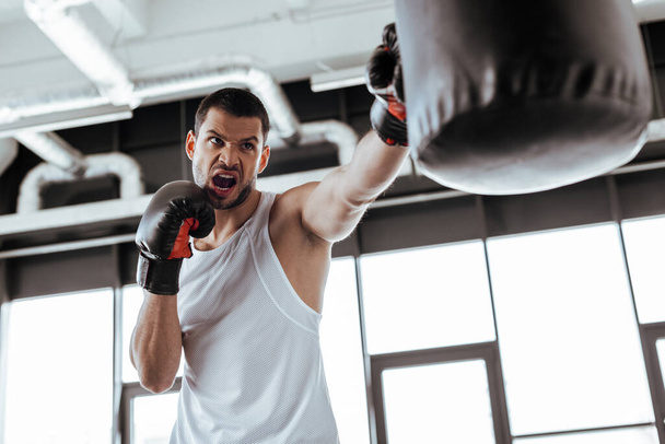 enfoque selectivo del hombre enojado en guantes de boxeo haciendo ejercicio con saco de boxeo
   - Foto, imagen