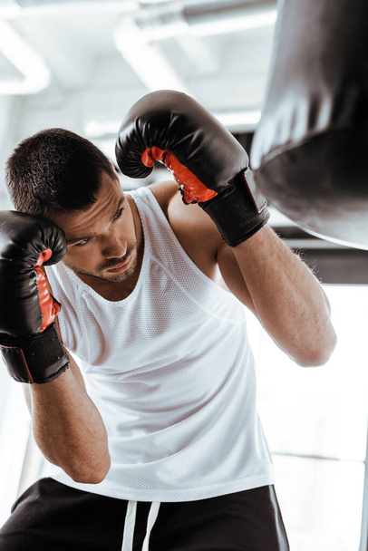 selective focus of handsome man in boxing gloves training with punching bag   - Foto, Imagem