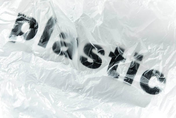 Zwart Plastic woord op doorzichtige witte wegwerp plastic zak. Milieuvervuiling probleem concept beeld met kopieerruimte - Foto, afbeelding