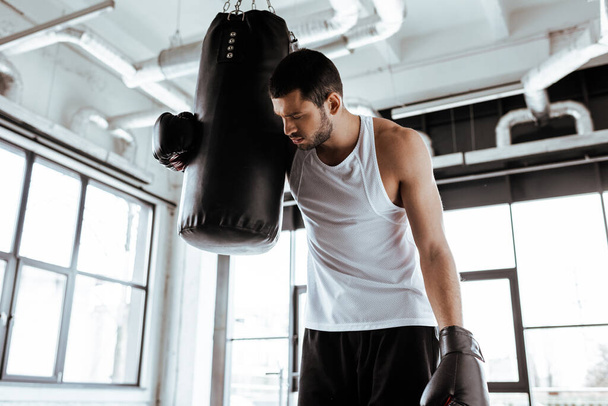 tired sportsman in boxing gloves standing near punching bag   - Photo, Image