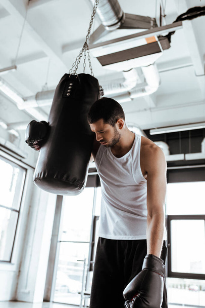 exhausted sportsman in boxing gloves standing near punching bag   - Foto, afbeelding