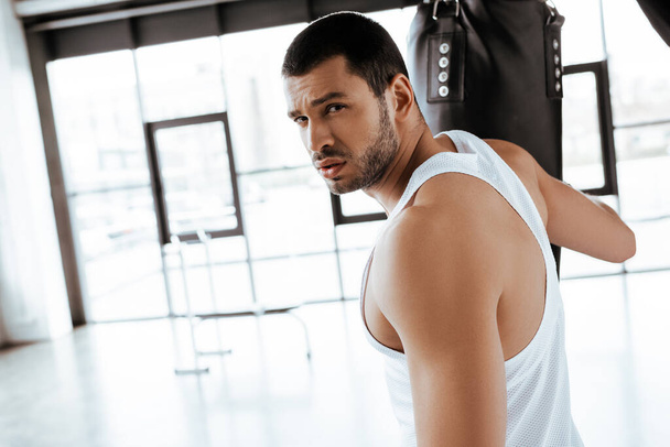 selective focus of handsome sportsman looking at camera near punching bag   - Фото, зображення