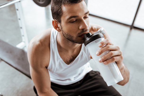 γενικά άποψη του αθλητή πόσιμο milkshake πρωτεΐνη, ενώ κρατώντας αθλητικό μπουκάλι στο γυμναστήριο  - Φωτογραφία, εικόνα