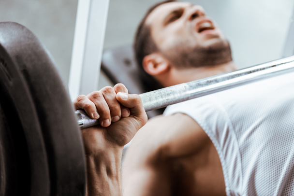 selective focus of emotional man exercising with barbell  - Foto, afbeelding