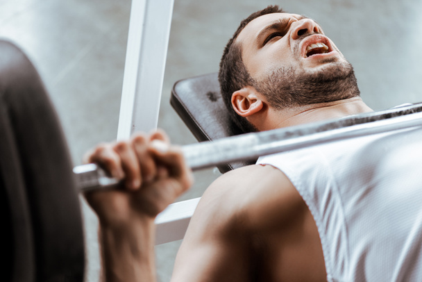 selective focus of emotional sportsman working out with barbell in gym  - Foto, Bild