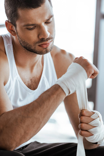 selective focus of handsome sportsman wrapping hand in sports bandage  - Foto, Imagem