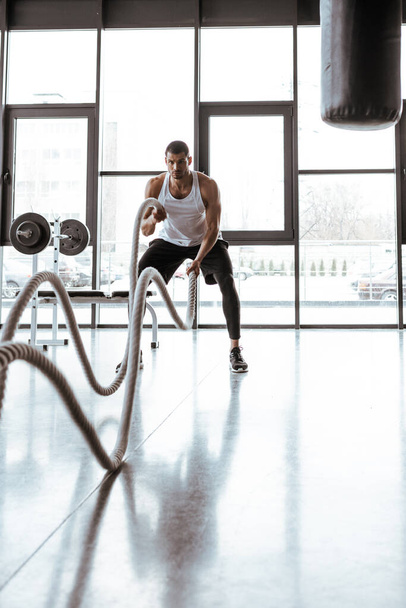selective focus of handsome sportsman exercising with battle ropes in modern gym  - Photo, Image