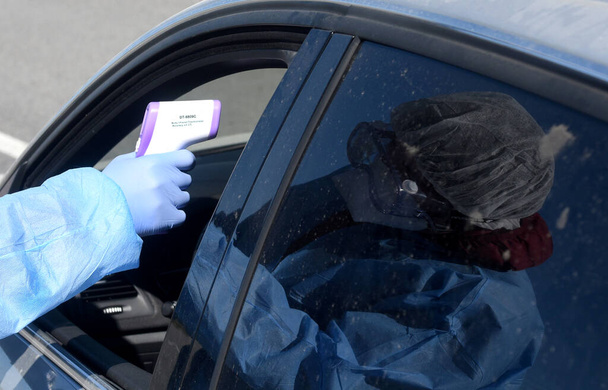 Lviv, Ukraine - April 10, 2020: Medical worker checks temperature of a driver on a checkpoint on the entrance to Lviv region. Quarantine restrictions in Ukraine over the coronavirus COVID-19 pandemic. - Photo, image