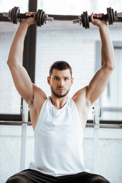 strong sportsman holding dumbbells above head while exercising in gym   - Photo, Image
