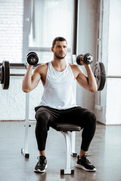 athletic man holding dumbbells while working out near barbell in gym   - Fotó, kép