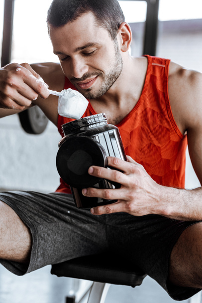 desportista feliz segurando frasco e olhando para colher de medição com pó de proteína
  - Foto, Imagem