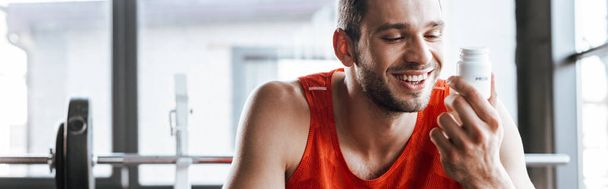Panoramaaufnahme eines glücklichen Sportlers mit Flasche mit probiotischem Schriftzug im Fitnessstudio  - Foto, Bild