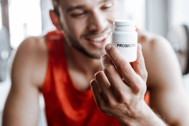 selective focus of happy sportsman holding bottle with probiotic lettering in gym  - Fotoğraf, Görsel