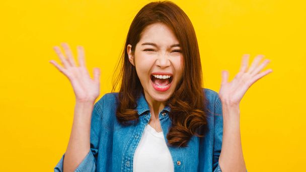 Portrait de jeune femme asiatique à l'expression positive, excitée criant, vêtue de vêtements décontractés et regardant la caméra sur fond jaune. Heureuse adorable femme heureuse se réjouit du succès
. - Photo, image