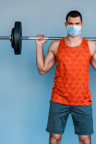 sportsman in medical mask exercising with barbell isolated on blue - Photo, Image
