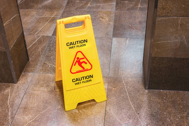 Señal amarilla precaución piso mojado con un hombre que cae en el pasillo del baño público
 - Foto, imagen