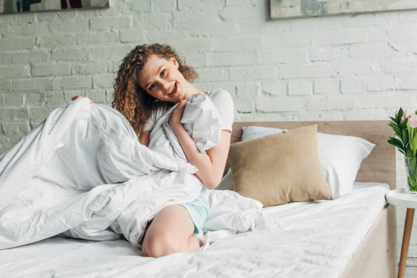 ελκυστικό χαρούμενο κορίτσι σε homewear κάθεται στο κρεβάτι το πρωί   - Φωτογραφία, εικόνα