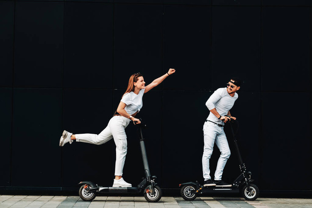 A girl and a guy are walking on electric scooters around the city, a couple in love on scooters. - Zdjęcie, obraz
