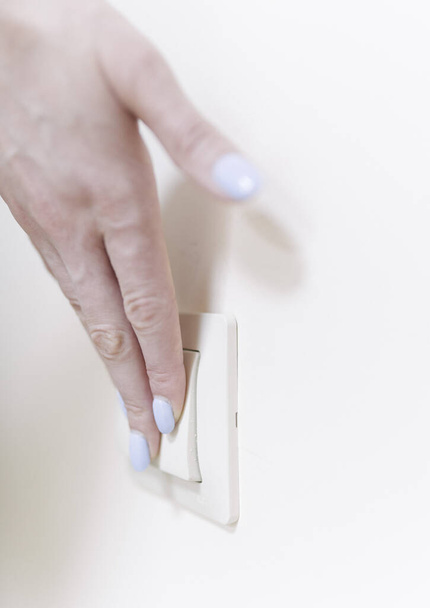 The woman turns off and turns on the light with a white switch on the wall, close-up. Control of utilities - Zdjęcie, obraz