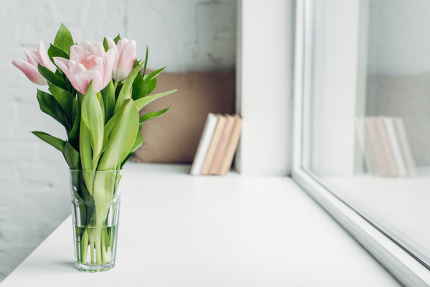 bouquet of pink tulips in glass on windowsill with books - Foto, imagen