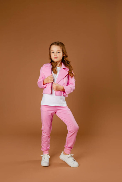 girl in a pink tracksuit does gymnastics and does exercises on a beige background - Foto, imagen
