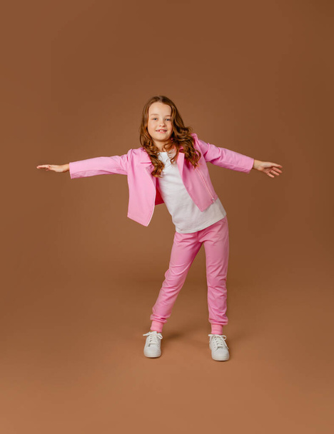 girl in a pink tracksuit does gymnastics and does exercises on a beige background - Φωτογραφία, εικόνα