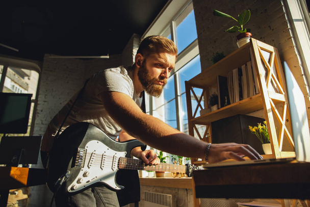 Caucasian musician playing guitar during online concert at home isolated and quarantined, tuning the stream - Fotografie, Obrázek