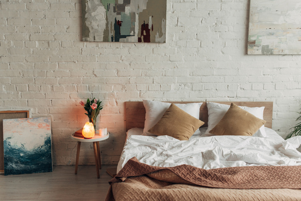 Schlafzimmereinrichtung mit Bett, Himalaya-Salzlampe, Tulpen und Gemälden  - Foto, Bild