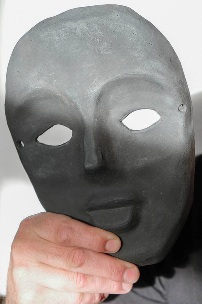 強い男の手に粘土で作られた黒いマスク。ウクライナで天気の良い朝の白い背景にマスク. - 写真・画像
