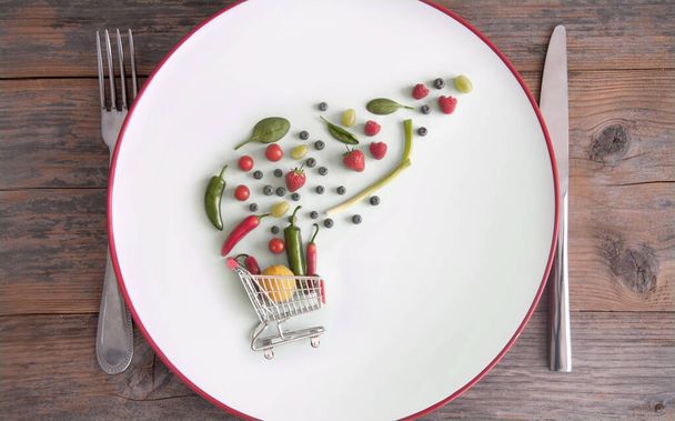 Small shopping cart trolley with fruits and vegetables on a plate - Photo, image