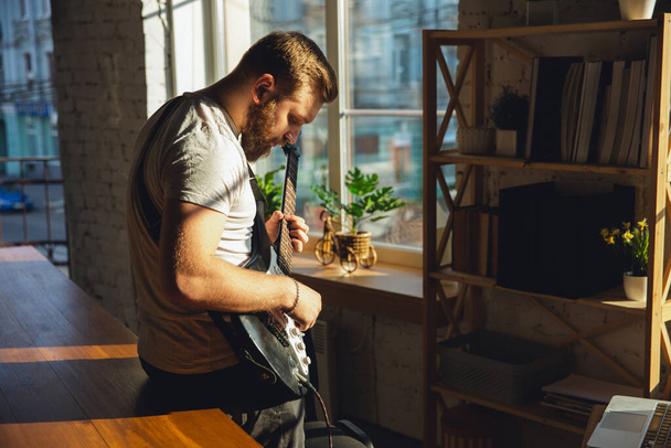 Caucasian musician playing guitar during online concert at home isolated and quarantined, impressive improvising in sunlight - 写真・画像