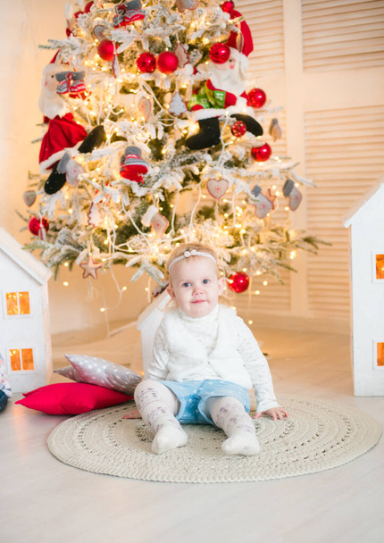 Cute little girl with blond hair plays  in a bright room decorated with Christmas garlands near the Christmas tree. Happy childhood. Christmas mood - Foto, imagen