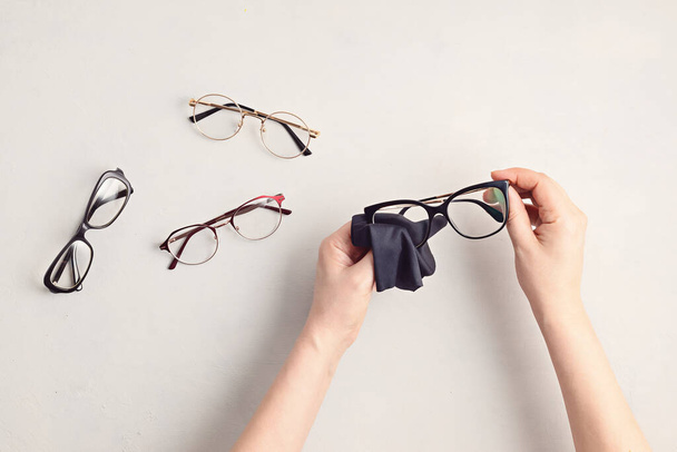 Woman hand cleaning eyeglasses. Optical store, glasses selection, eye test, vision examination at optician, fashion accessories concept. Top view, flat lay - Photo, Image