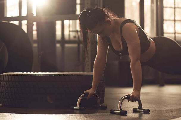 Young woman does push-ups with sports equipment in the gym. Real Workout Candid fitness Girl - Foto, Bild