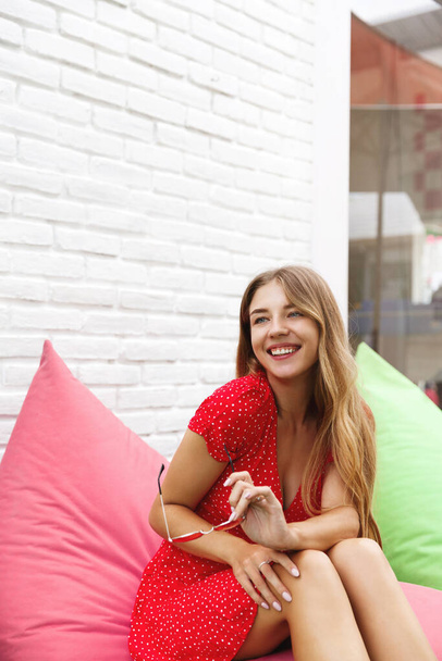 Leisure, summer vacation and journey concept. Beautiful lady traveller, woman sit on bean bag chair outside cafe, waiting for ice latte on hot day, laughing and smiling, travel around world - Foto, afbeelding