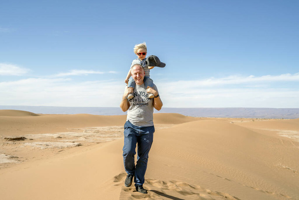 Πατέρας περπατώντας με piggypacked 2 ετών γιος μέσω Σαχάρα έρημο στο Μαρόκο, Αφρική - Φωτογραφία, εικόνα