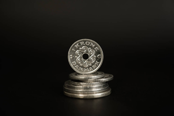 Eine dänische Kronenmünze steht auf einem Stapel Münzen vor schwarzem Hintergrund. - Foto, Bild