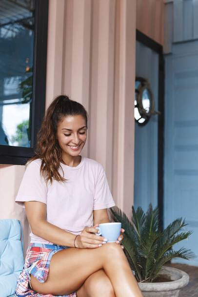 Stay safe, comfort and relaxation concept. Vertical shot of romantic, pretty woman smile at cup of tea, feel comfort, fill leisure with hapy small moment during lockdown at home on self-quarantine - Fotó, kép